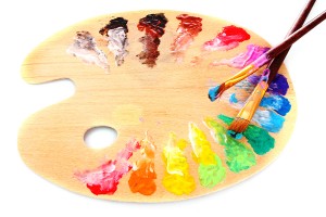 wooden art palette with blobs of paint and a brush on white background